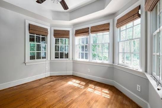 Empty sunlit room with hardwood floors and bay windows fitted with woven bamboo Roman shades.