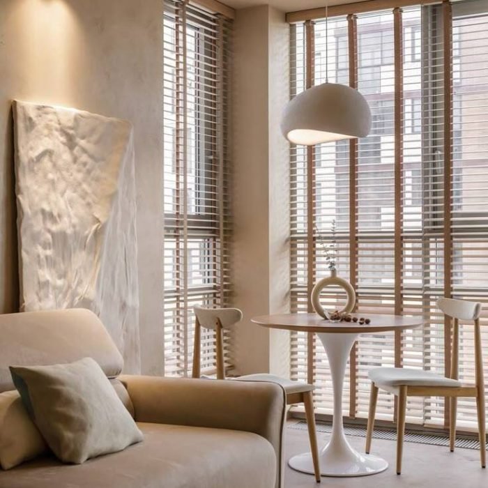 Modern apartment nook with wooden Venetian blinds, small dining table, and armchair.